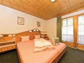 A bedroom with a wooden bed, a nightstand, a dresser, a window with curtains, and two framed pictures on the wall. - Appartements Lärchenhof, (Samnaun-Compatsch) by Interhome (Samnaun)