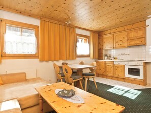 A cozy room with a wooden ceiling, a dining table with chairs, a sofa, and a kitchen area with wooden cabinets and a stove. - Appartements Lärchenhof, (Samnaun-Compatsch) by Interhome (Samnaun)