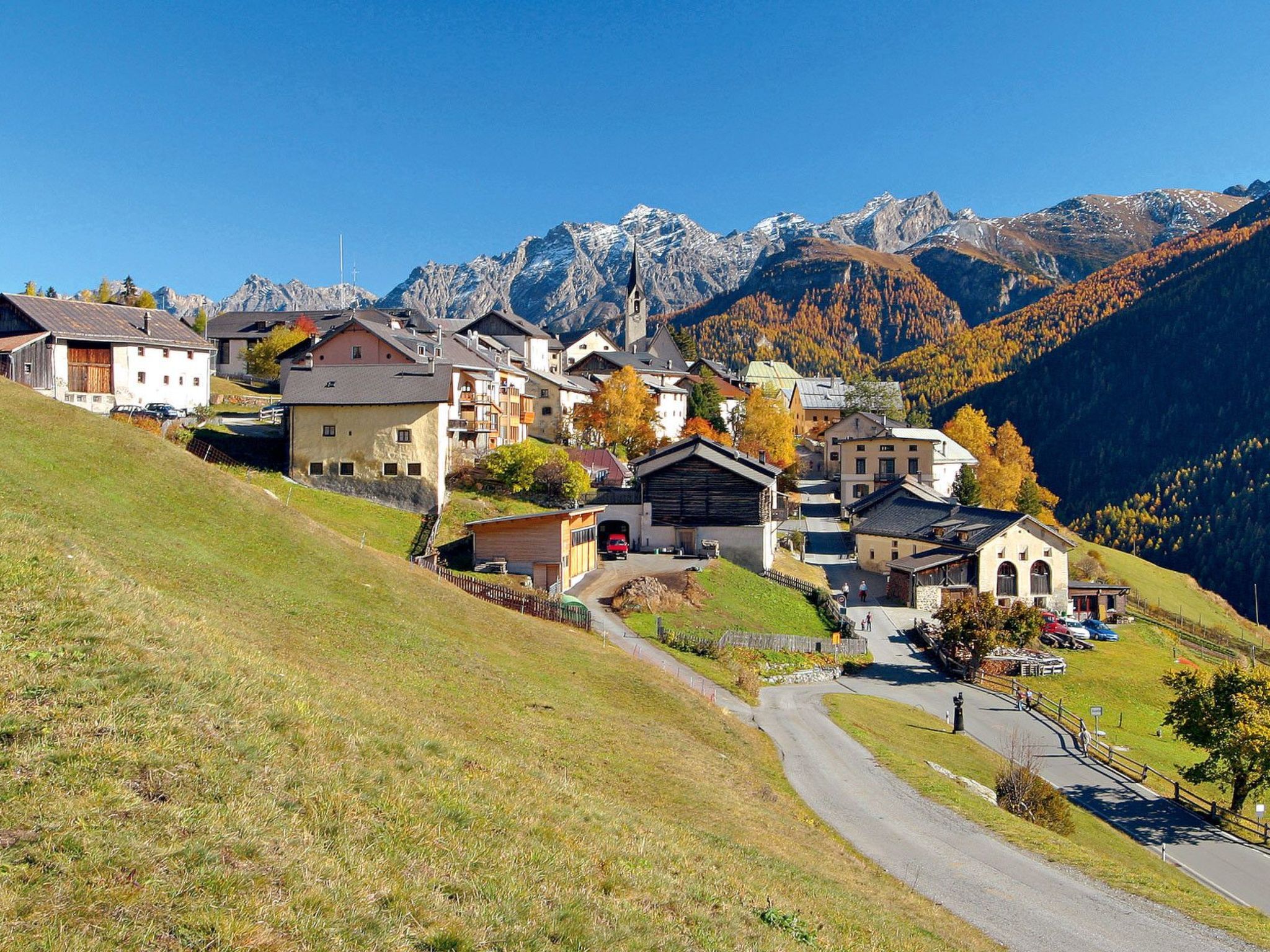 A village with traditional buildings, a church, and a road leading uphill.