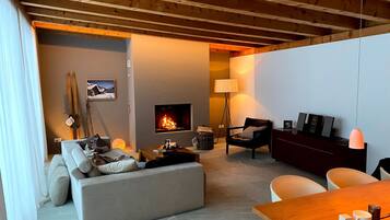 A cozy living room with a fireplace, a sofa, a dining table, and a lamp.