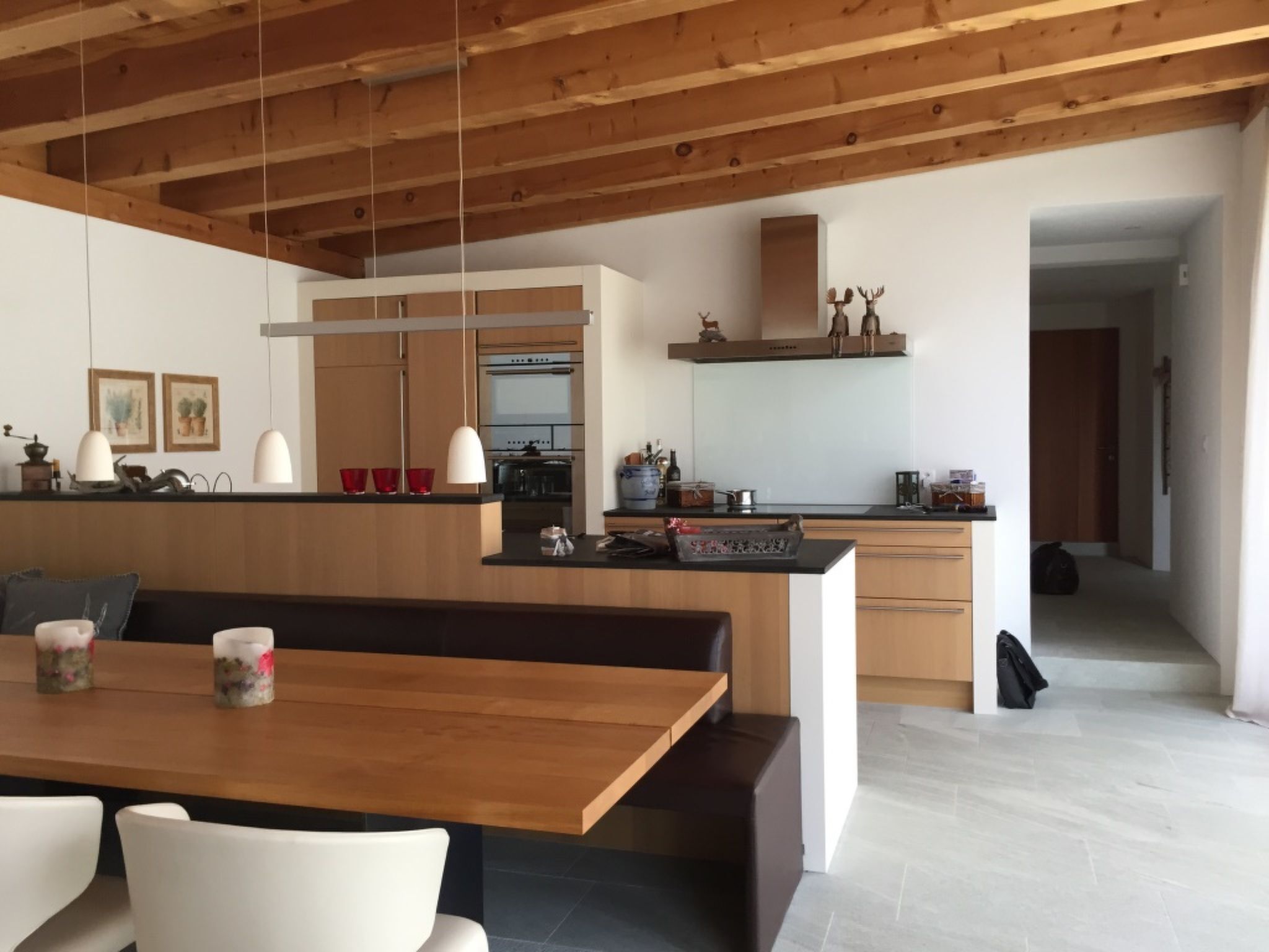 Una cocina moderna con vigas de madera, una zona de comedor con banco y un pasillo que conduce a otra habitación.