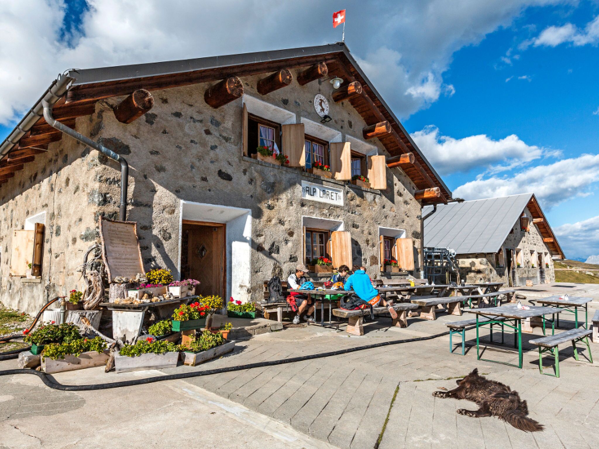 A stone building with a wooden roof, outdoor seating, and a flag.