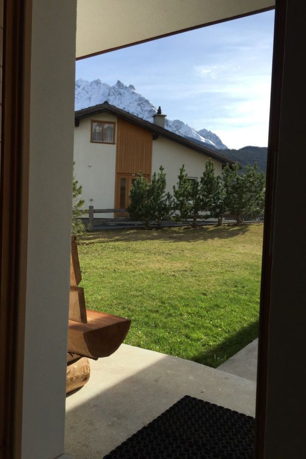 Une vue d’un bâtiment avec une porte en bois et une cour verdoyante qui mène à une chaîne de montagnes.