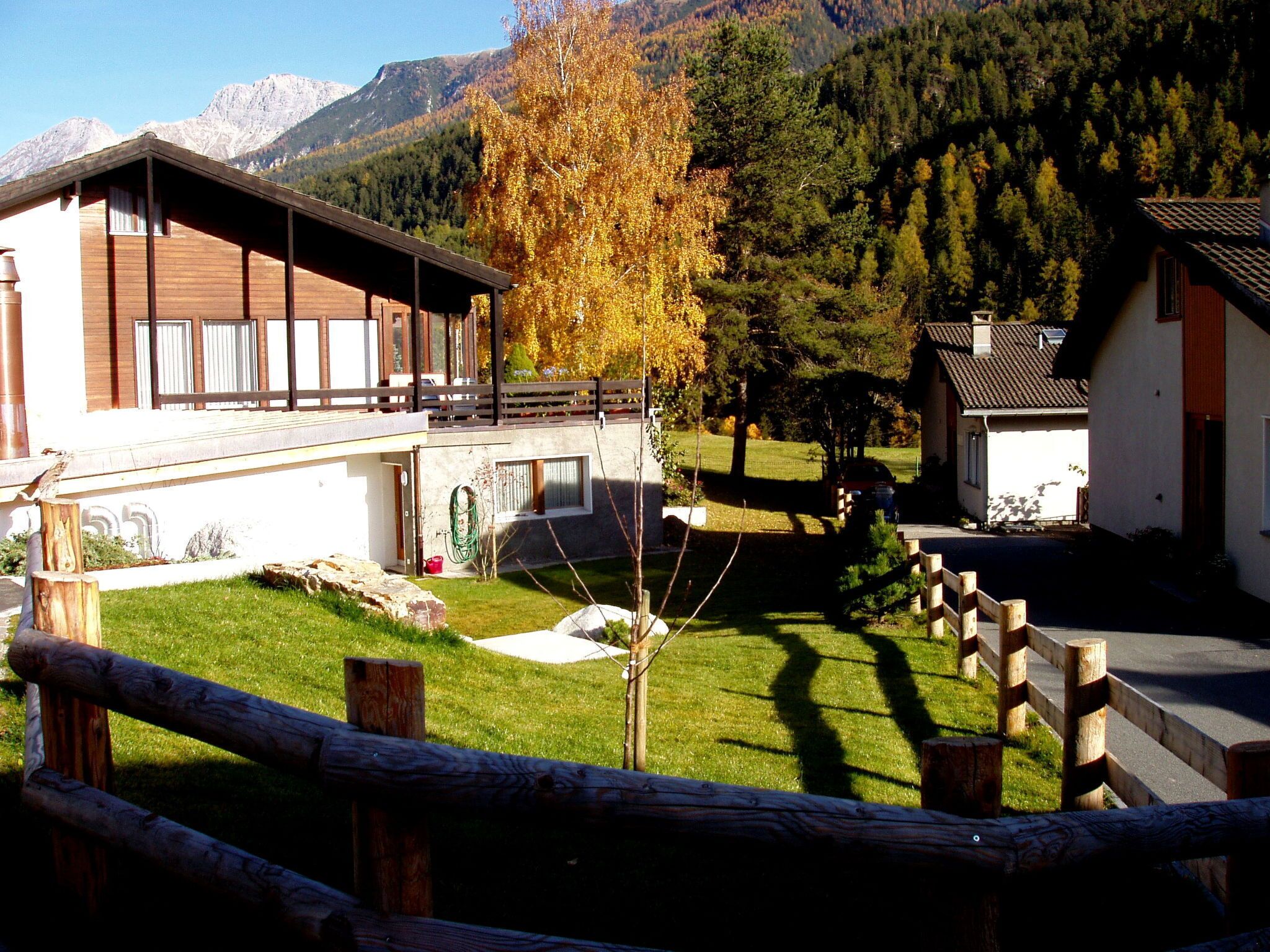 A modern building with a wooden deck, a small garden, and a mountain backdrop.