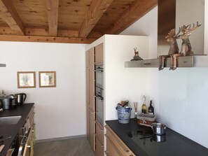 Een moderne keuken met houten balken, een inbouwoven en een plank met decoratieve hertenbeeldjes.
