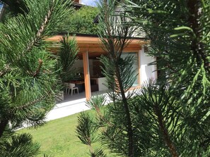 A modern house with a covered patio, a lawn, and a dining area visible through the windows. - Manaröl 607, (Scuol) by Interhome (Scuol)