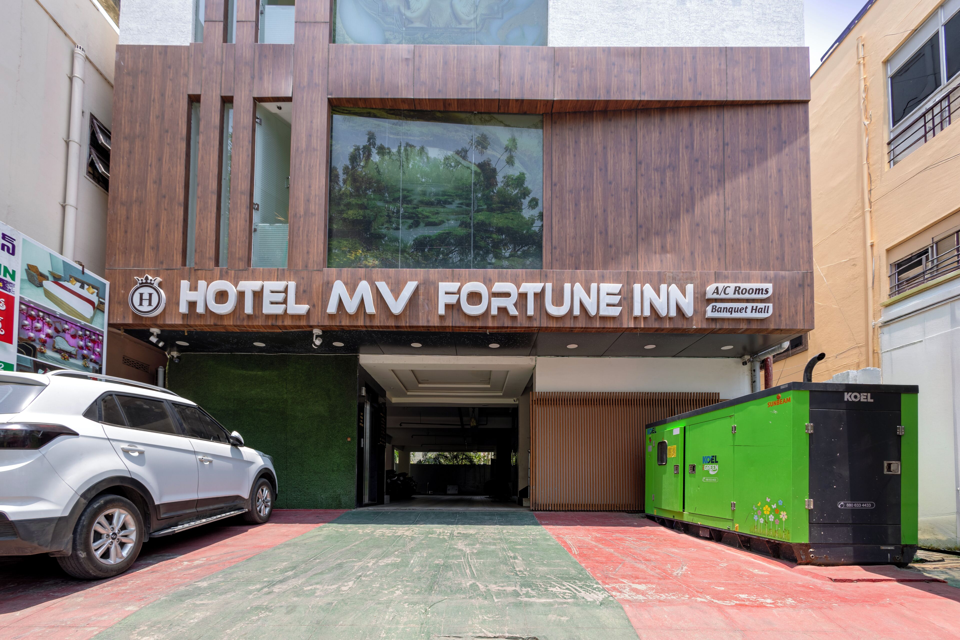 Edifici modern amb un cartell que indica 'Hotel MV Fortune Inn', habitacions amb aire condicionat i una sala de banquet.