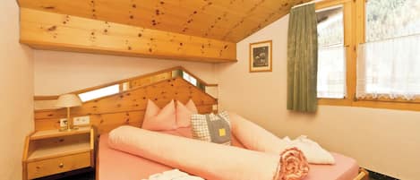 Une chambre confortable avec un plafond en bois, un lit avec une literie rose, une table de chevet, une fenêtre avec des rideaux et un petit tableau accroché au mur.