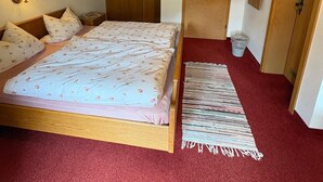 A bedroom with a wooden ceiling, a bed with floral bedding, a red carpet, and a small rug. - Rauher Kopf Vacation Rental, 50 m², 1–4 people, 2 bedrooms, 2 showers/toilets, kitchen (Bischofswiesen)