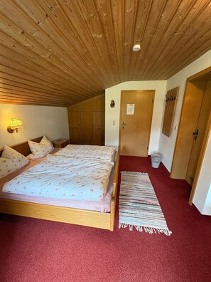 Ein Schlafzimmer mit Holzboden, einem Bett mit Blumenmuster-Bettwäsche, einem roten Teppich und einem kleinen Läufer.
