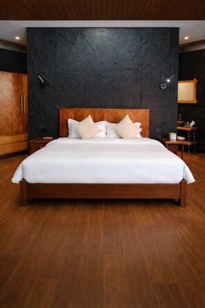 A large bed with a wooden headboard in a room with dark walls and wooden flooring.