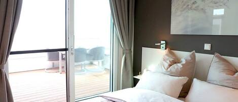 A hotel room with a bed, a window with curtains, a view of the outside, and a wall-mounted artwork.