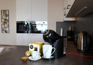 Eine moderne Küche mit Kaffeemaschine, einer Packung Dolce Gusto Kapseln, einer Tasse und einem Untertasse.