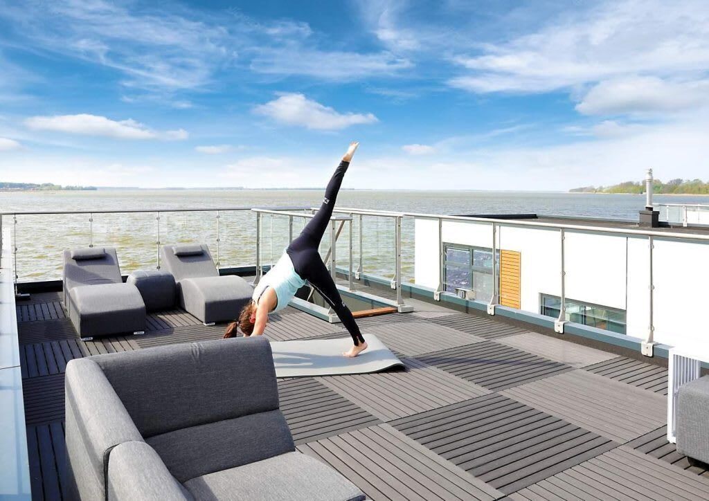 Une personne effectuant une posture de yoga sur une terrasse avec vue sur l’eau.