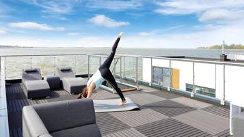 Une personne effectuant une posture de yoga sur une terrasse avec vue sur l’eau.
