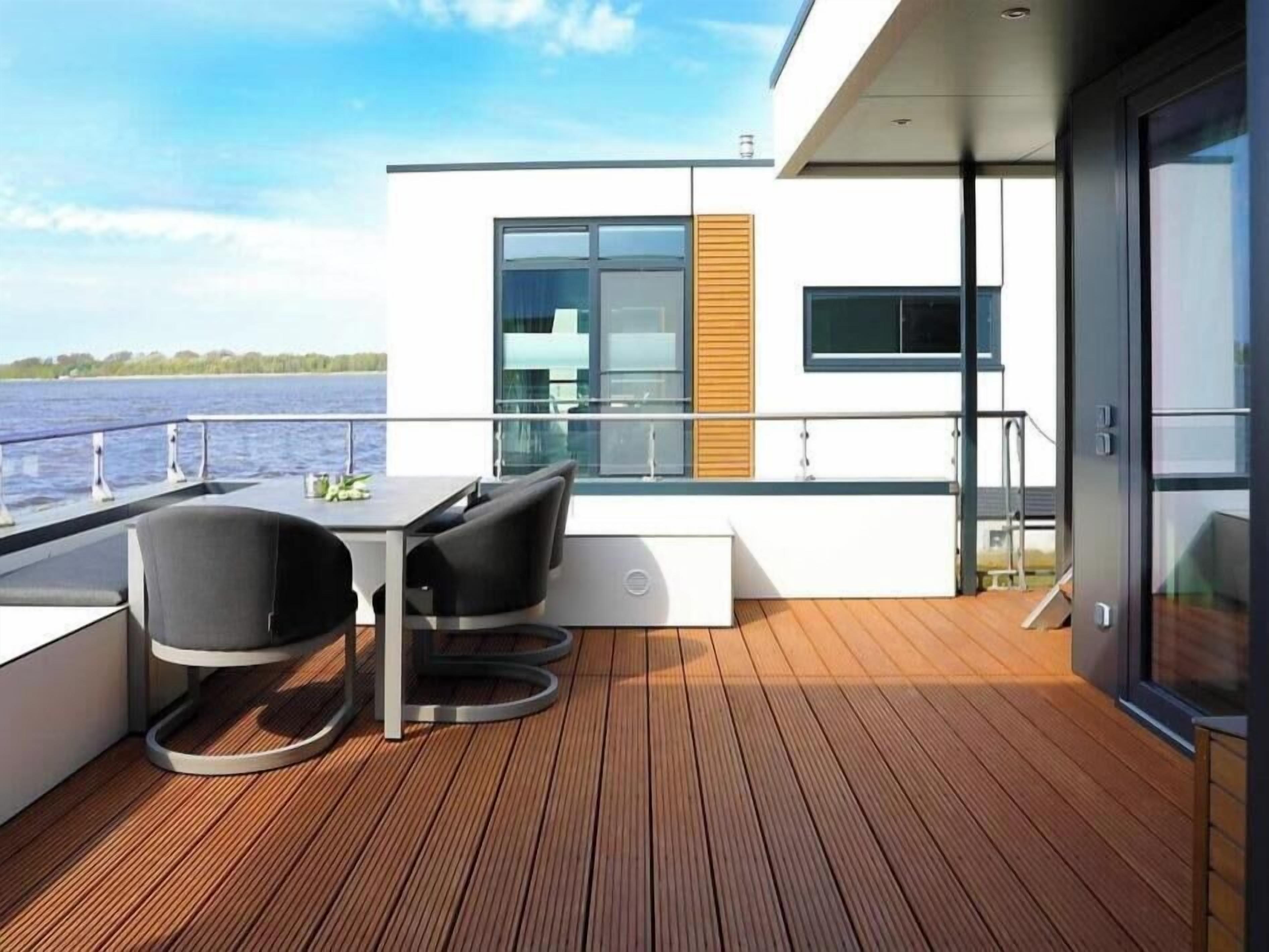 Eine moderne Terrasse mit Tisch und Stühlen, mit Blick auf ein Gewässer.