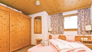 Une chambre à coucher avec un lit en bois, une armoire, un miroir et une fenêtre avec des rideaux.