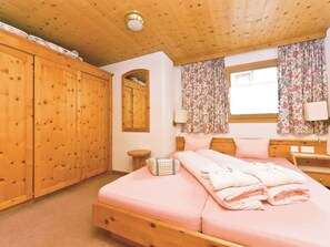 A bedroom with a wooden bed, a wardrobe, a mirror, and a window with curtains. - Appartements Lärchenhof, (Samnaun-Compatsch) by Interhome (Samnaun)