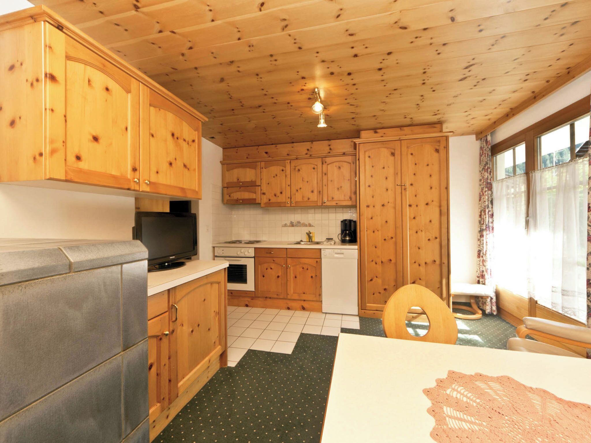A kitchen with wooden cabinets, a refrigerator, a coffee maker, and a window with curtains.