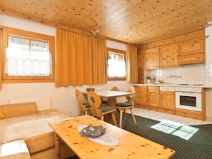 A cozy room with a wooden ceiling, a dining table with chairs, a sofa, and a kitchen area with wooden cabinets and a stove. - Appartements Lärchenhof, (Samnaun-Compatsch) by Interhome (Samnaun)