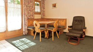Une pièce avec une table et des chaises en bois, un banc, un fauteuil en cuir et une fenêtre avec des rideaux.
