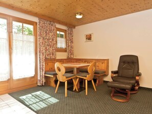A cozy room with a wooden bench, a dining table with chairs, a leather armchair, and a window with floral curtains. - Appartements Lärchenhof, (Samnaun-Compatsch) by Interhome (Samnaun)