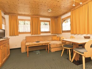 A cozy room with a sofa, a small table, a dining table with chairs, and a television on a cabinet. - Appartements Lärchenhof, (Samnaun-Compatsch) by Interhome (Samnaun)