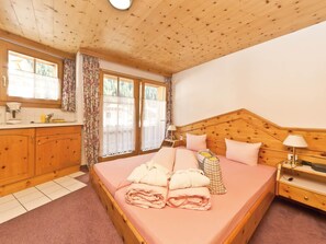 A bedroom with a wooden headboard, a bed with pink bedding, a bedside table with a lamp, and a window with curtains. - Appartements Lärchenhof, (Samnaun-Compatsch) by Interhome (Samnaun)