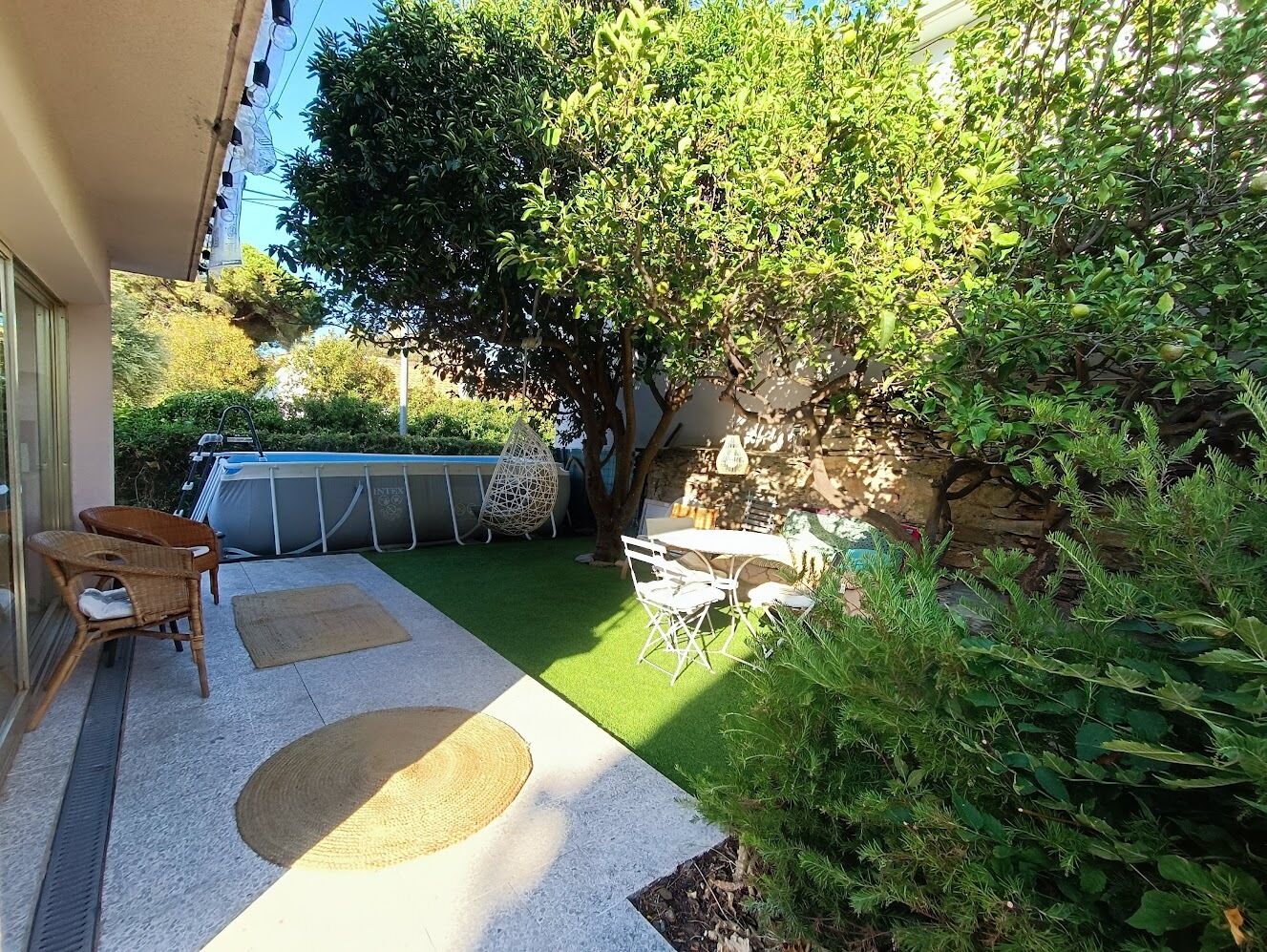 A patio area with a small table and chairs, a pool, and surrounding greenery.