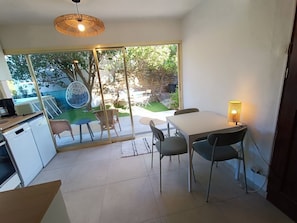 A modern kitchen with a dining area, large windows, and a view of an outdoor garden. - 100 meters from the ocean—apartment for 3 people (Santa-Maria-di-Lota)