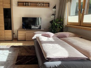 Ein Schlafzimmer mit Bett, Fernseher, einer Kommode mit Dekoration und einem Fenster mit Vorhängen.