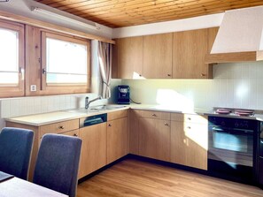 Eine moderne Küche mit Holzausstattung, einer integrierten Spülmaschine, einem Herd und einem Fenster mit Vorhängen.