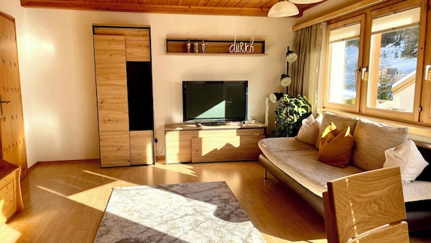 Uma sala de estar acolhedora com teto de madeira, uma TV de tela plana, um sofá com almofadas, uma mesa de centro e um tapete.