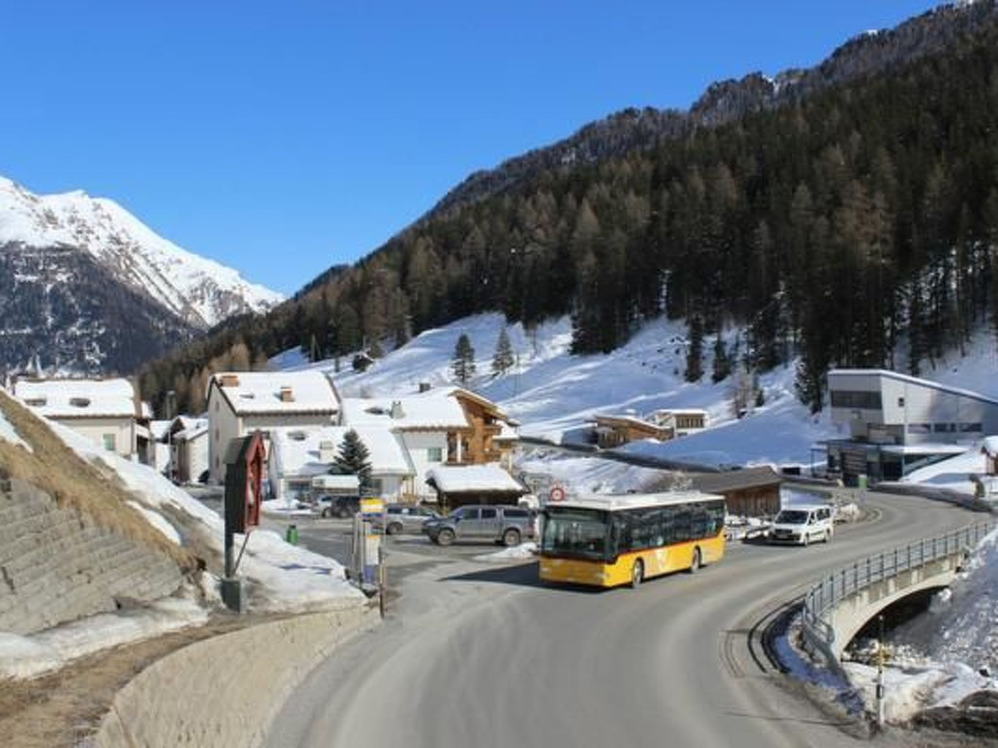 Un pueblo cubierto de nieve en la montaña, con un autobús en una carretera sinuosa.