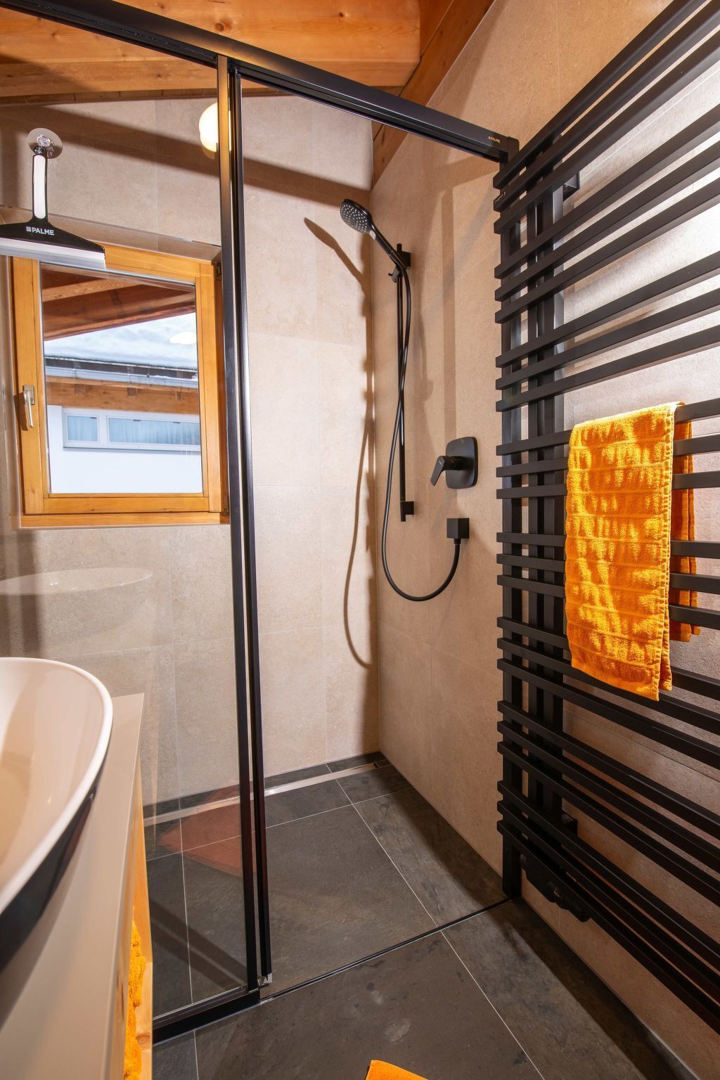 A modern bathroom with a glass shower enclosure, a white sink, and a towel rack with a yellow towel.