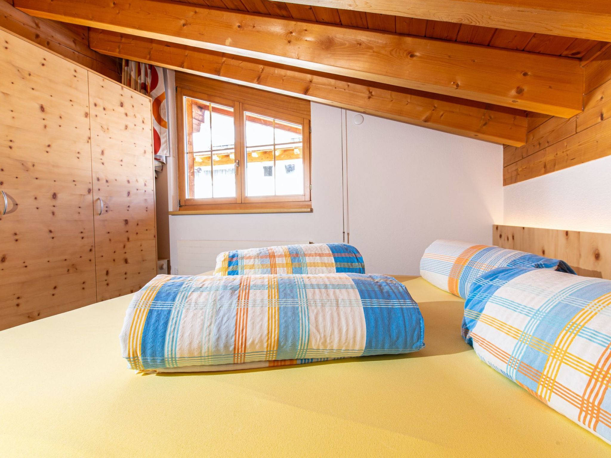 Un dormitorio con dos camas, paredes de madera, una ventana y un techo con vigas de madera.
