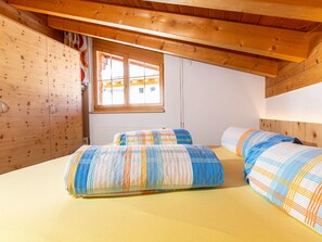 Un dormitorio con dos camas, paredes de madera, una ventana y un techo con vigas de madera.