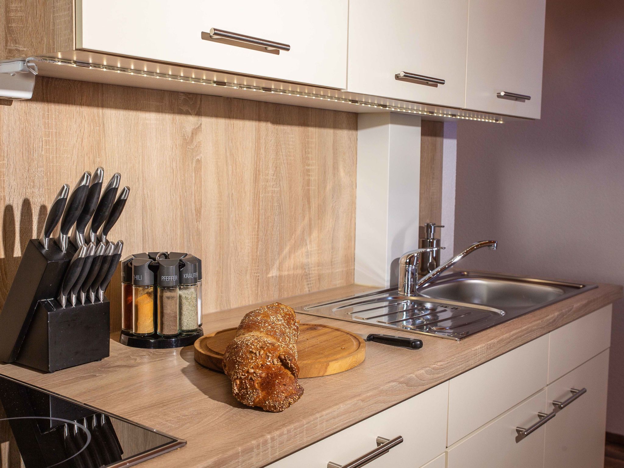 A modern kitchen with a wooden countertop, a bread loaf, a knife block, and spice jars.