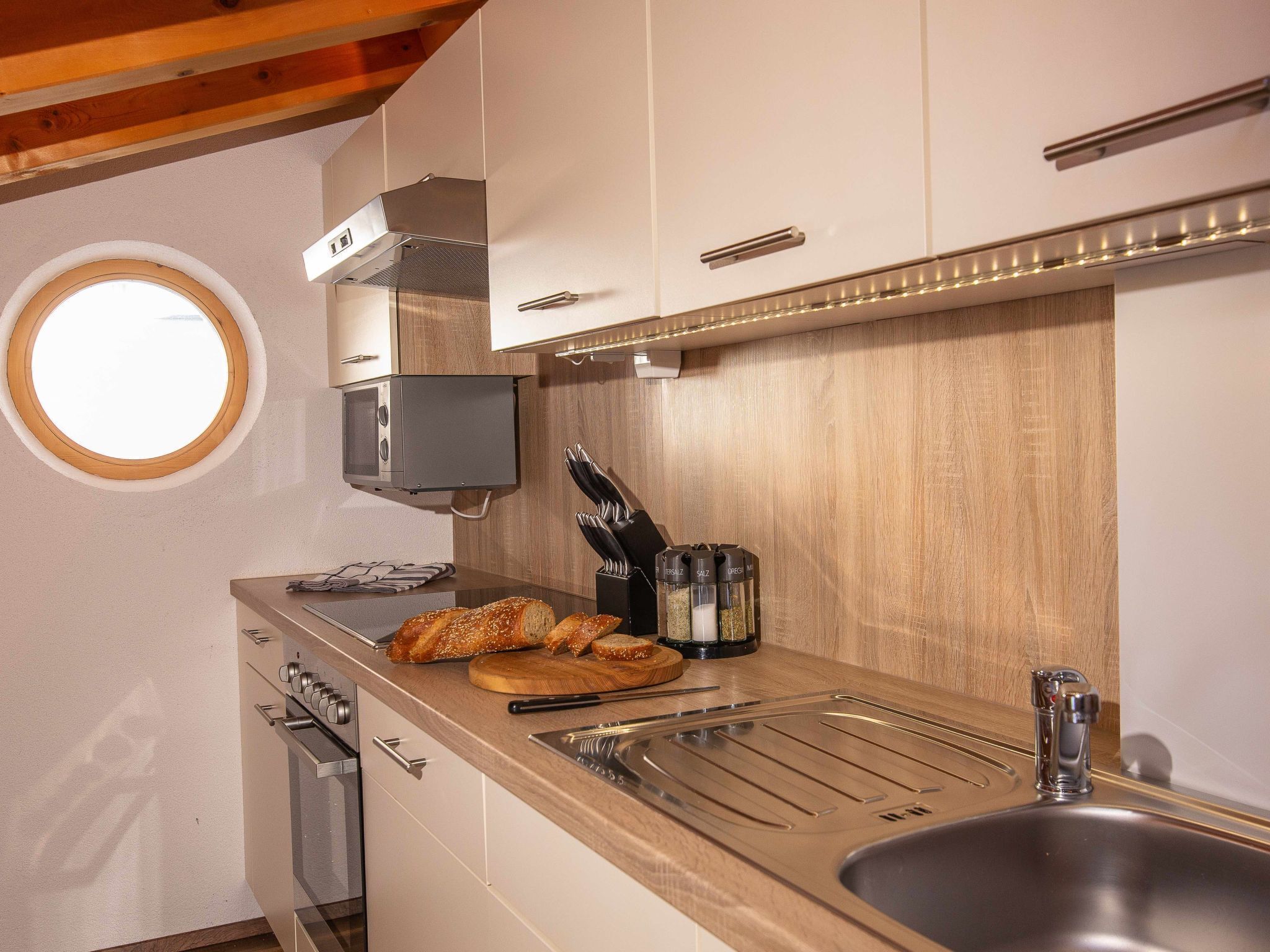 Una cucina con una finestra circolare, forno a incasso, lavello e piano di lavoro in legno.