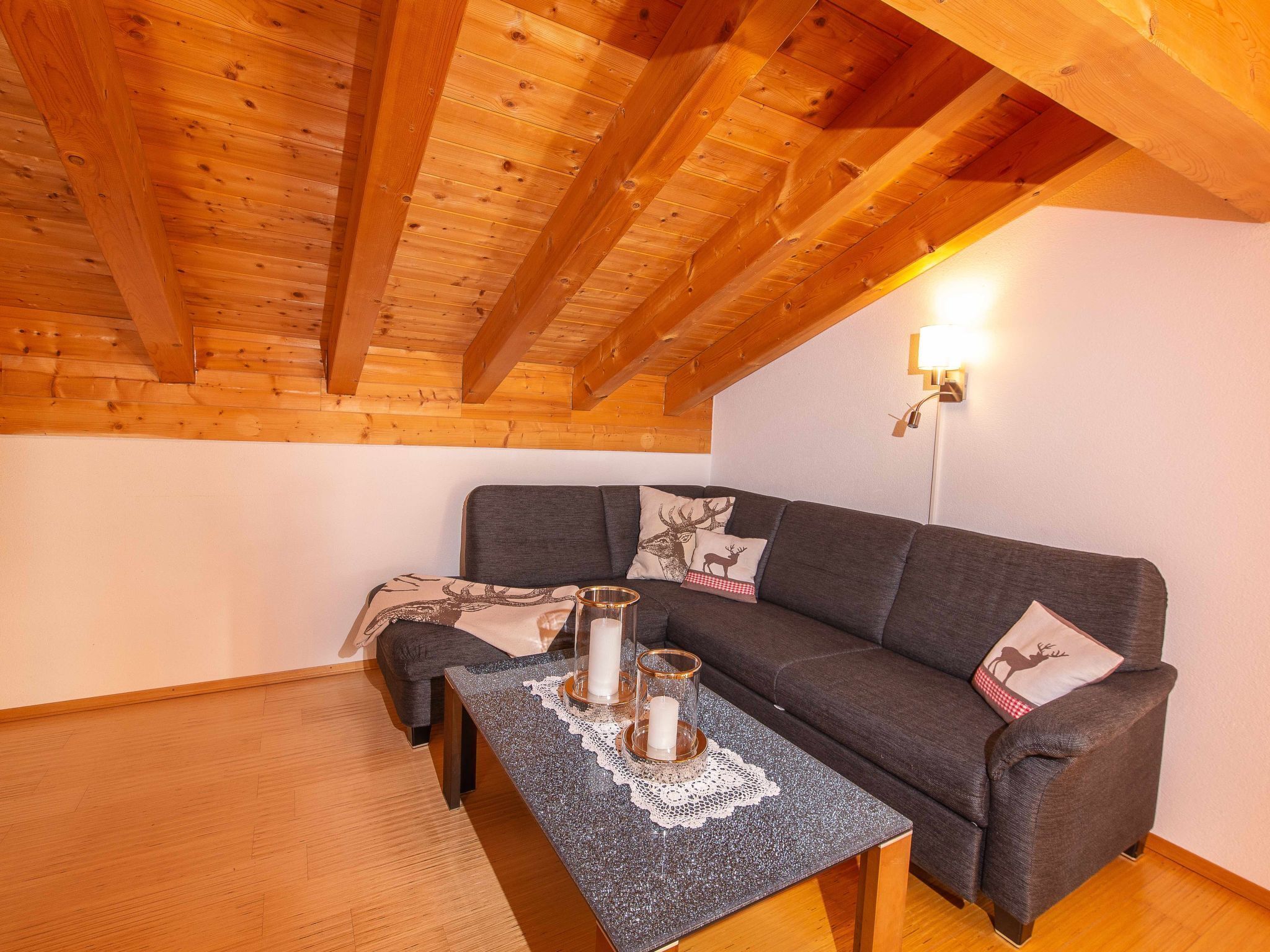 Una stanza accogliente con soffitto in legno, un divano grigio con cuscini decorativi e un tavolo con candele.