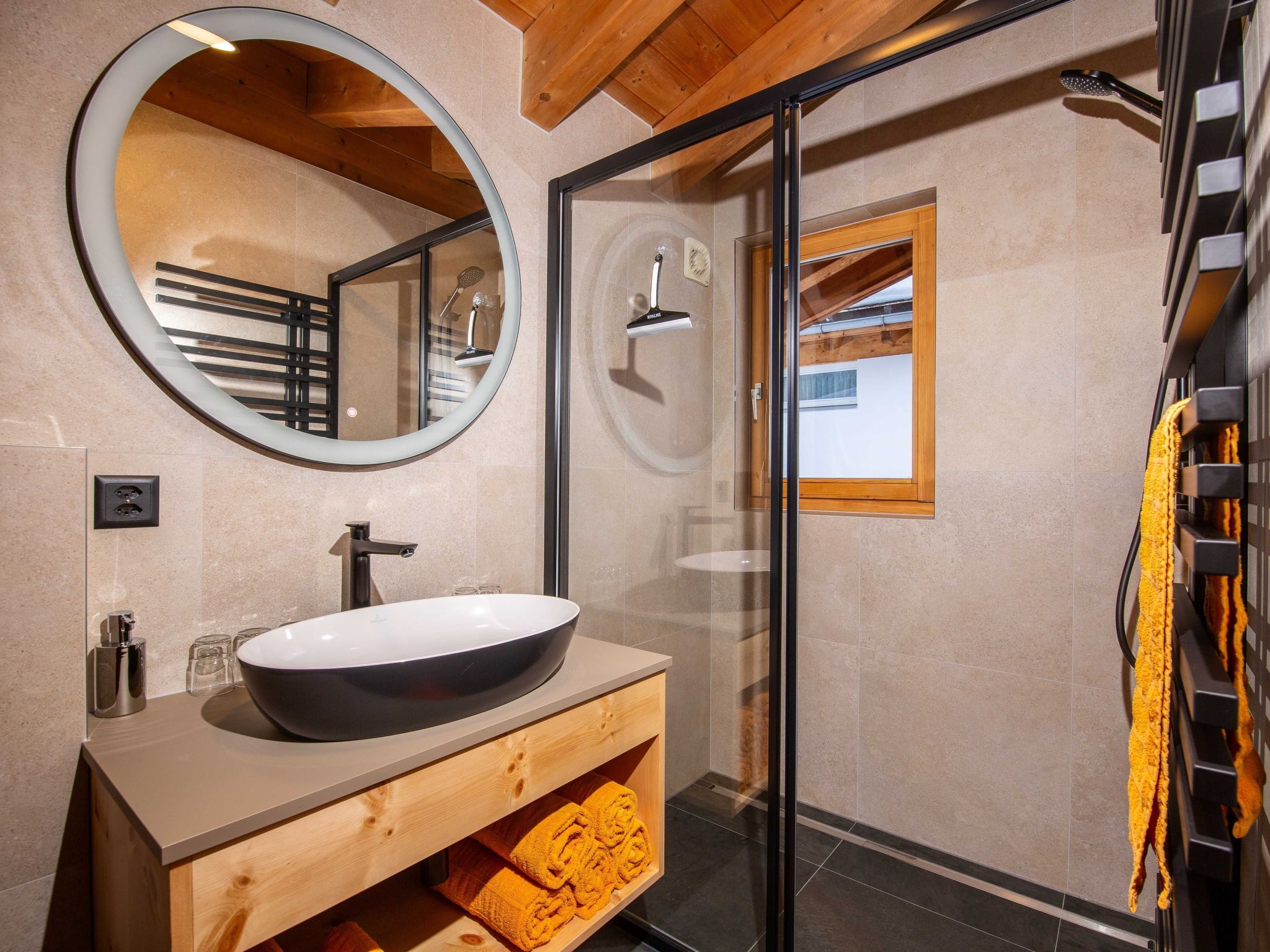 Ein modernes Badezimmer mit einem großen, ovalen Waschbecken, einem runden Spiegel, einer Duschkabine aus Glas und einem Holz-Waschtisch.