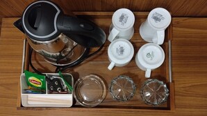 Un cajón con una cafetera, seis tazas blancas, un sobre de té Lipton y dos tapas de vidrio.