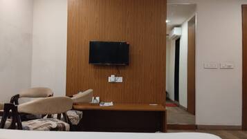 Una habitación de hotel con una cama, un escritorio, una silla, un televisor montado en un panel de madera y una puerta que da a otra habitación.
