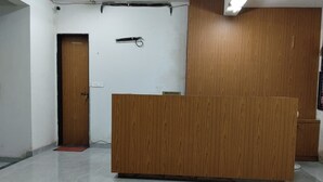 Mostrador de recepción en el vestíbulo de un hotel, con detalles de madera, un letrero del área de recepción y una puerta a la izquierda.