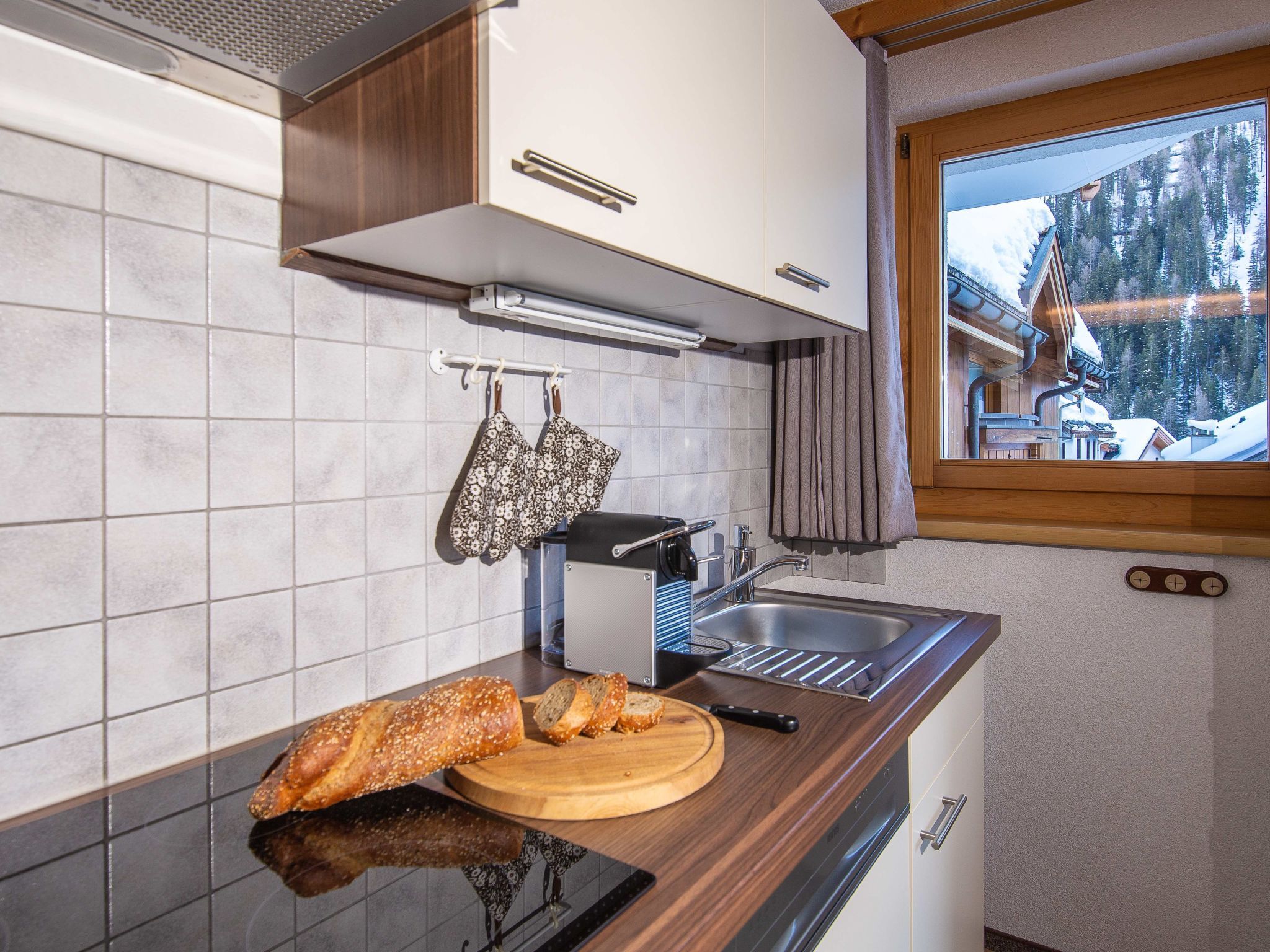 Una cucina con un piano di lavoro in legno, una pagnotta, un tostapane e una finestra con vista su un paesaggio innevato.