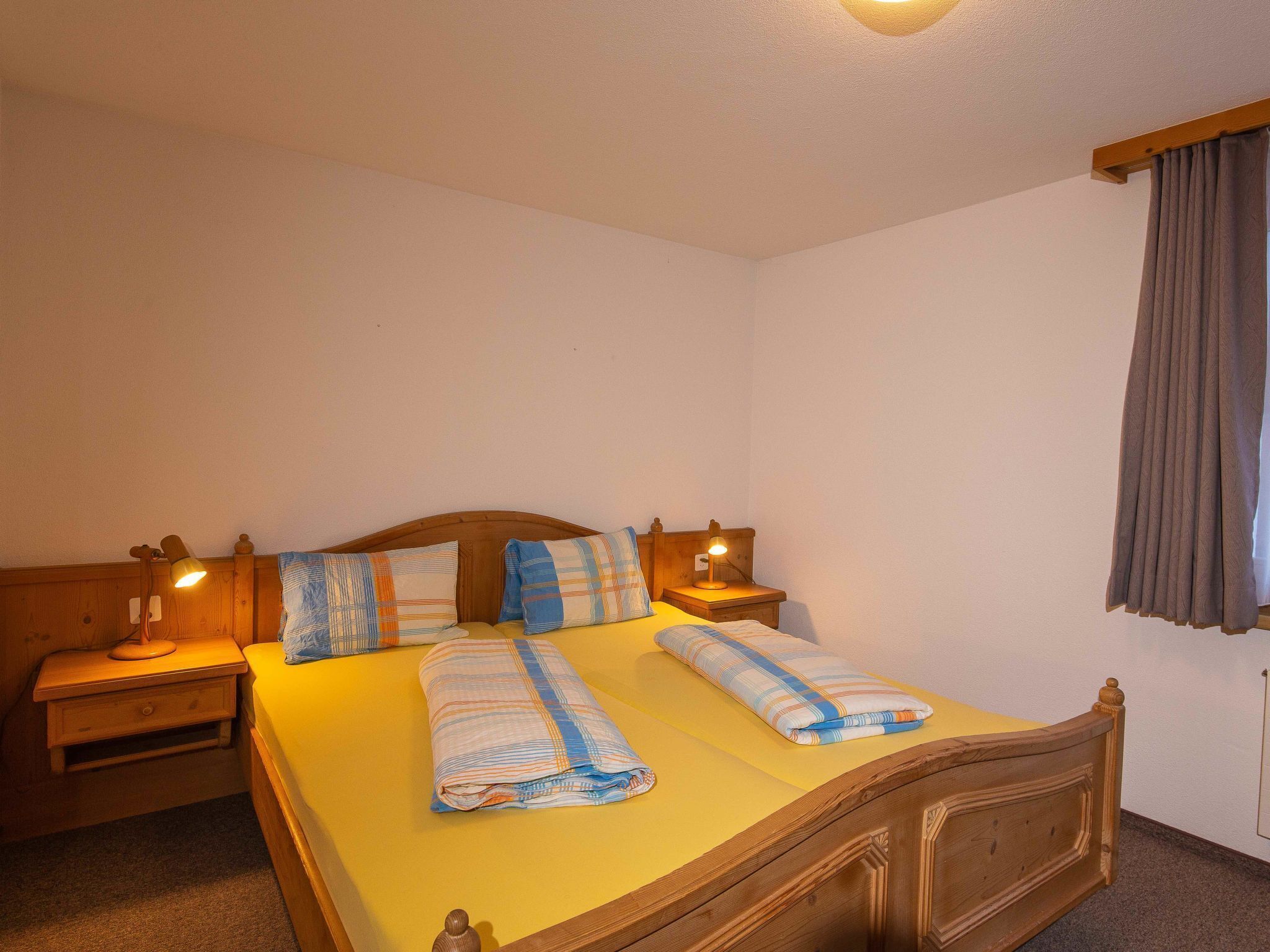 Un lit double avec une tête de lit en bois, deux tables de chevet avec des lampes et une fenêtre avec des rideaux.
