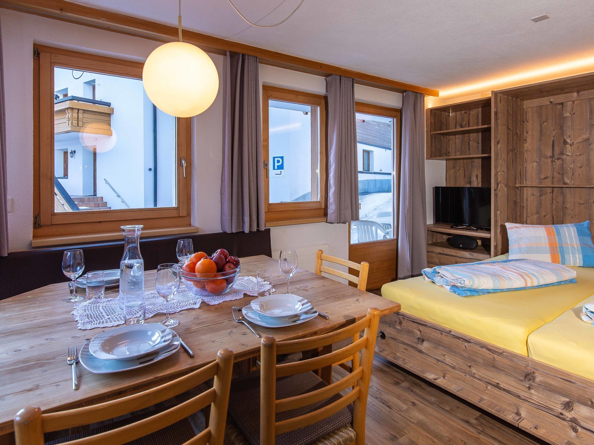 Una stanza con un tavolo da pranzo apparecchiato per due persone, un letto con una coperta colorata e un televisore su una mensola di legno.