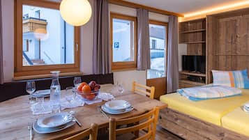Una stanza con un tavolo da pranzo apparecchiato per due persone, un letto con una coperta colorata e un televisore su una mensola di legno.