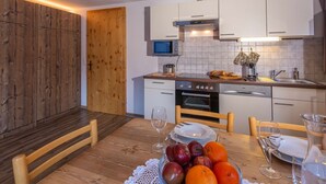 A modern kitchen with white cabinets, a microwave, and a stove. There is a dining table with plates, a bowl of fruit, and a glass of water.