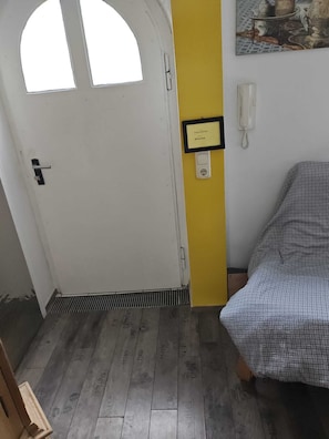 Una habitación con puerta blanca, pared amarilla, cama con colcha estampada, teléfono blanco y un cuadro en la pared.